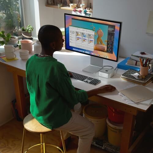 Person in green shirt working at a desk with a computer